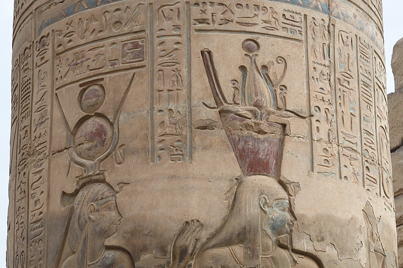 38 MAK_6351pp.jpg - La dea Hathor indossa una corona composita con corna di mucca, il disco solare e il cobra. Il faraone una corona con fiori di loto aperti in cima, rappresentante la purezza, la creazione e la rinascita. Sotto i fiori si trova un vaso nemset dotato di beccuccio, utilizzati per versare libagioni e in vari riti di purificazione che poggia su corna di ariete ricurve, accompagnate da cobra sacri (uraeus) che simboleggiano la protezione e l'autorità reale.